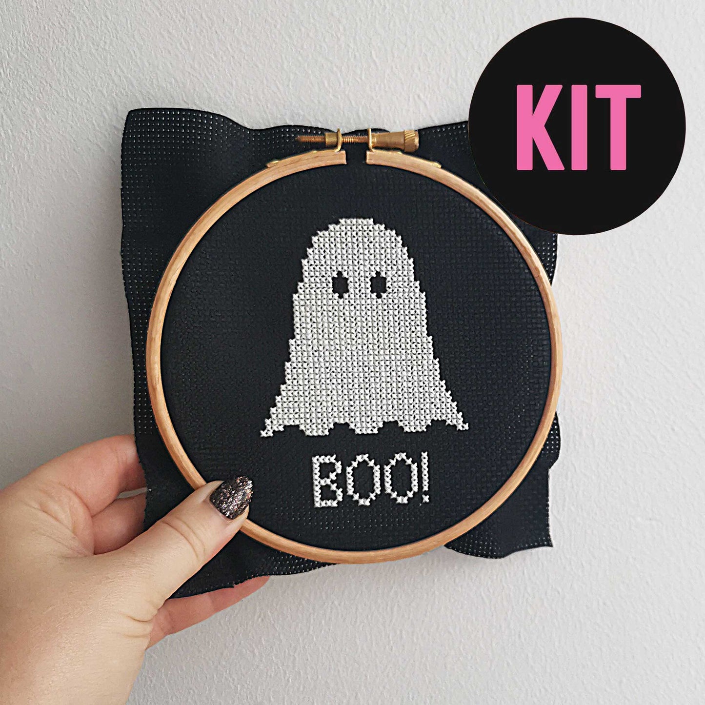 A cute ghost cross stitched in white on black fabric above the word 'boo'.