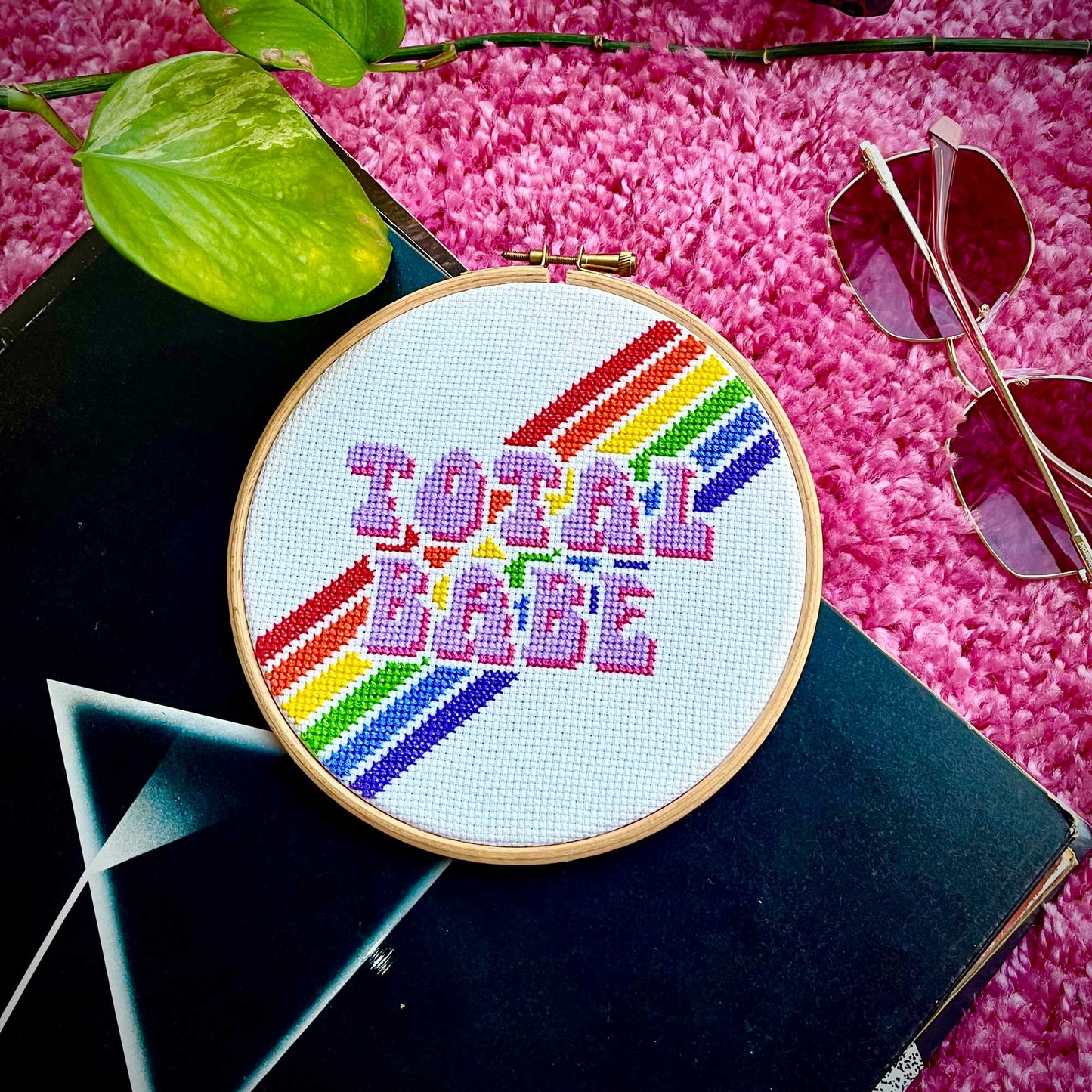 A rainbow cross stitch is on top of a pile of records.